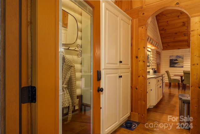 hall featuring wooden walls, lofted ceiling, and hardwood / wood-style flooring