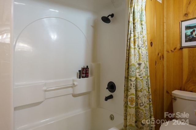 bathroom featuring shower / bathtub combination with curtain, wooden walls, and toilet