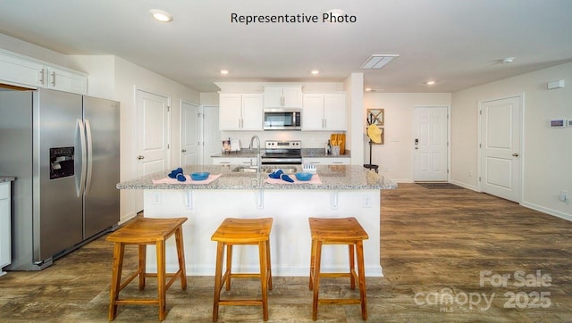 kitchen with light stone countertops, white cabinetry, stainless steel appliances, and an island with sink