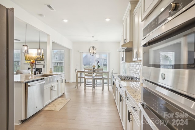 kitchen featuring hanging light fixtures, light hardwood / wood-style flooring, white cabinetry, appliances with stainless steel finishes, and a wealth of natural light