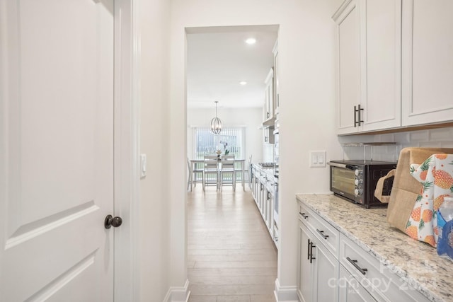 interior space featuring light wood-type flooring, tasteful backsplash, white cabinetry, decorative light fixtures, and light stone countertops