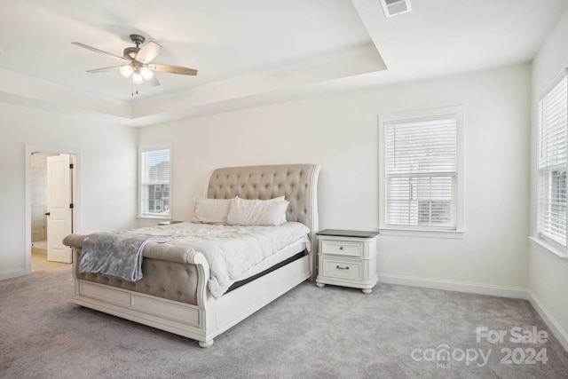 carpeted bedroom with ceiling fan, a raised ceiling, and ensuite bath