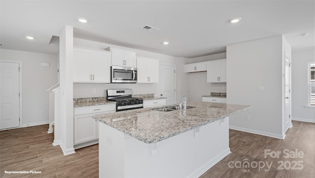 kitchen with a kitchen island with sink, white cabinets, sink, appliances with stainless steel finishes, and light stone counters