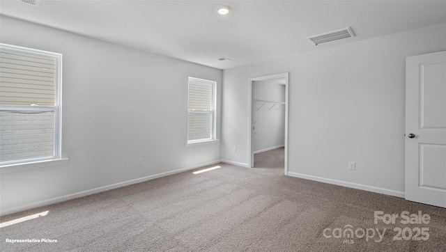 unfurnished bedroom featuring carpet, multiple windows, a spacious closet, and a closet