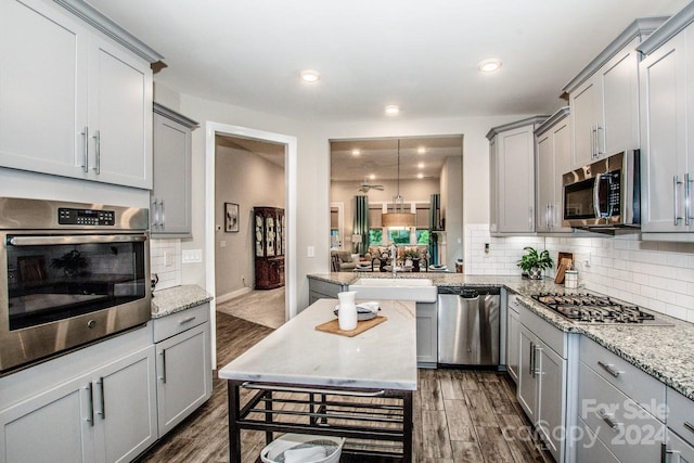 kitchen with dark hardwood / wood-style flooring, pendant lighting, stainless steel appliances, and light stone counters