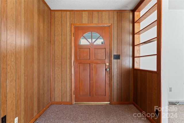 carpeted entrance foyer featuring a textured ceiling and wood walls