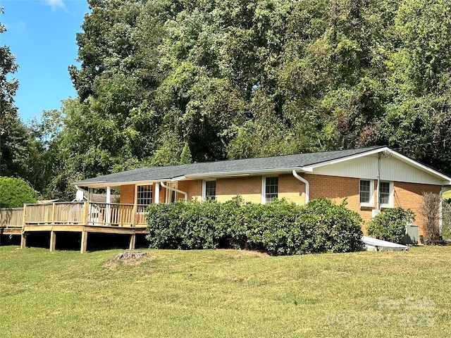 rear view of house with brick siding, a lawn, and a wooden deck