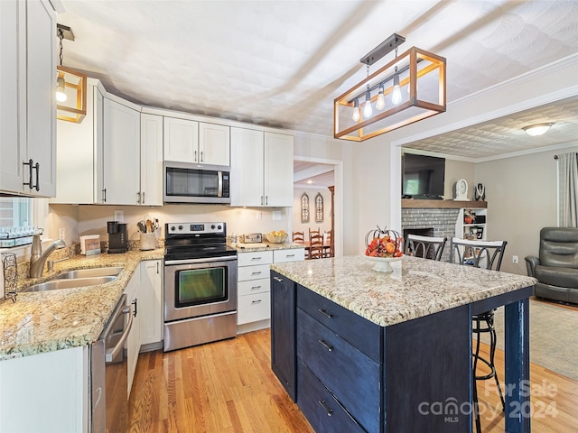 kitchen with sink, a brick fireplace, decorative light fixtures, appliances with stainless steel finishes, and light hardwood / wood-style floors