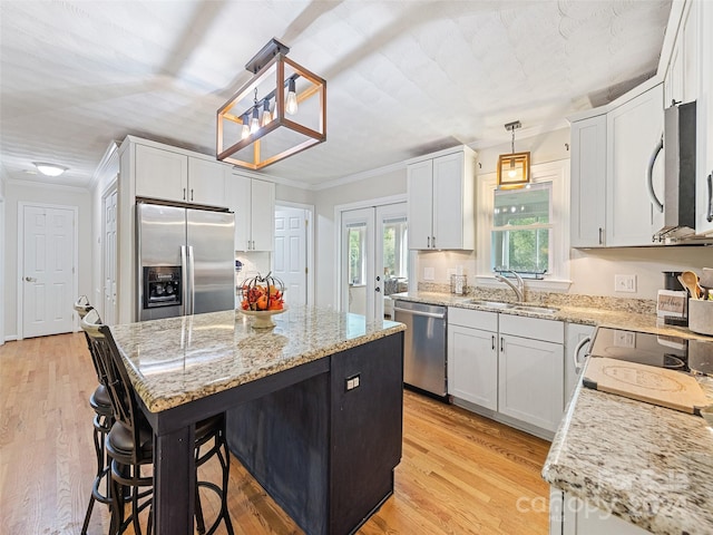 kitchen featuring hanging light fixtures, white cabinetry, stainless steel appliances, light wood-type flooring, and sink