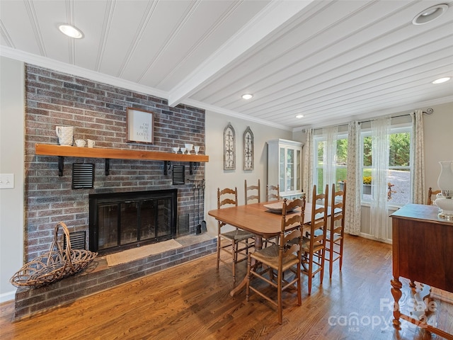 dining area with wood-type flooring, a fireplace, crown molding, and beamed ceiling