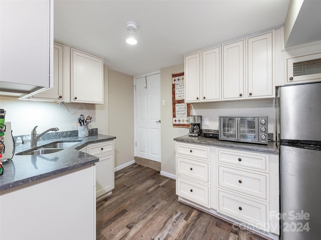 kitchen with stainless steel fridge, dark stone countertops, dark wood-type flooring, white cabinets, and sink