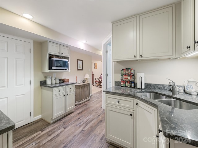 kitchen featuring dark stone counters, wood-type flooring, stainless steel microwave, and sink