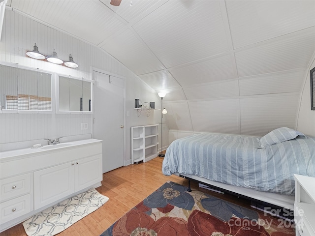 bedroom with light wood-type flooring, vaulted ceiling, ceiling fan, and wooden walls