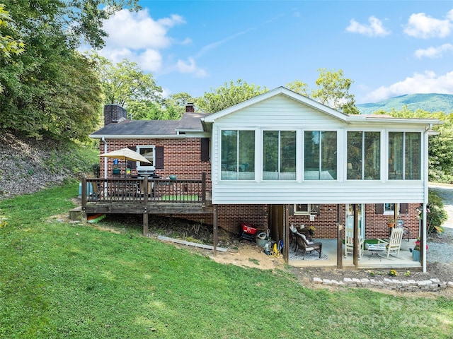 rear view of house featuring a sunroom, a patio area, a deck with mountain view, and a yard