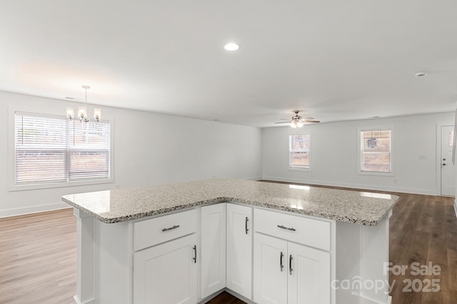 kitchen featuring light stone counters, ceiling fan with notable chandelier, pendant lighting, light hardwood / wood-style flooring, and white cabinetry