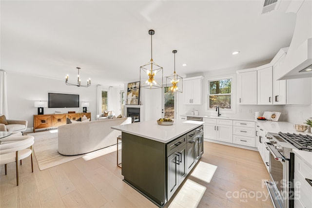 kitchen featuring white cabinetry, a center island, sink, high end stainless steel range oven, and pendant lighting