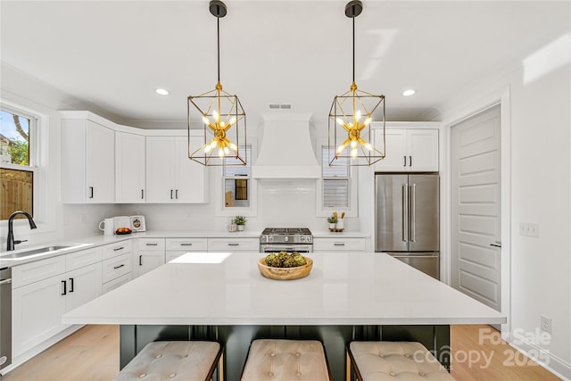 kitchen with a kitchen bar, custom exhaust hood, sink, high quality appliances, and hanging light fixtures