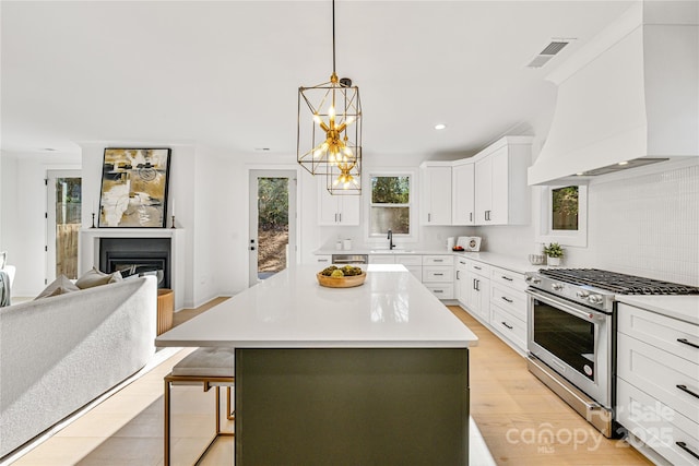 kitchen with premium range hood, sink, a center island, stainless steel stove, and white cabinetry