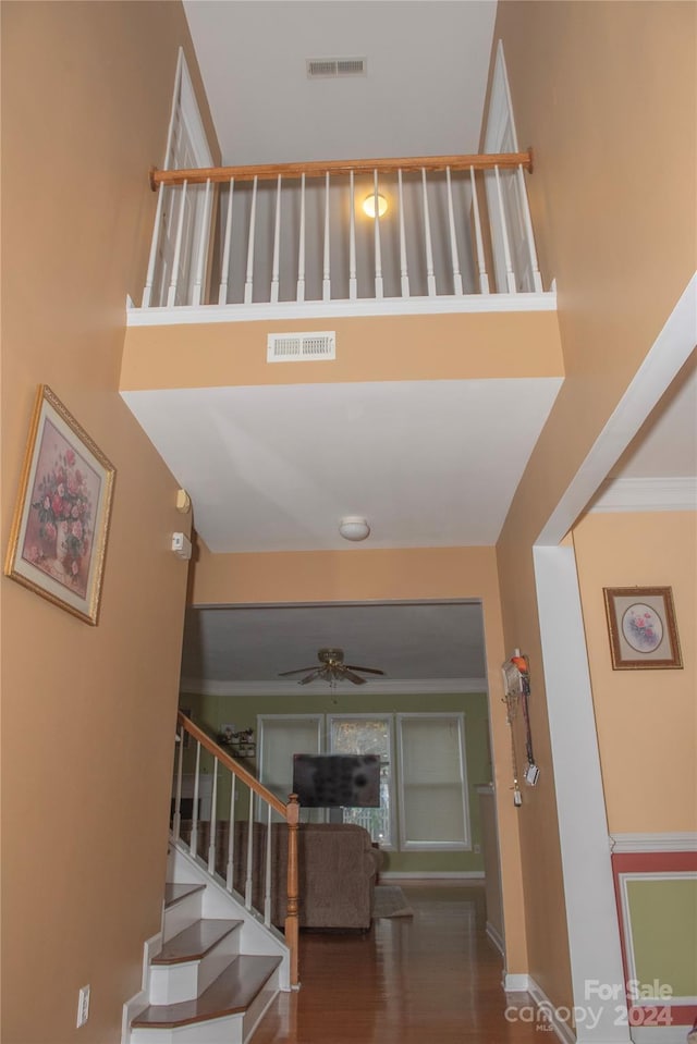 stairway with ceiling fan, wood-type flooring, crown molding, and a high ceiling