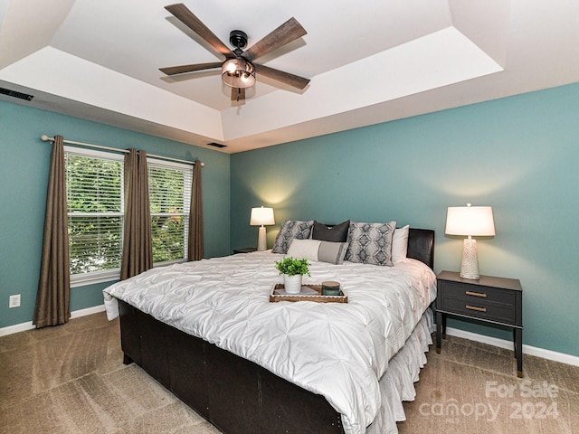 carpeted bedroom featuring ceiling fan and a raised ceiling