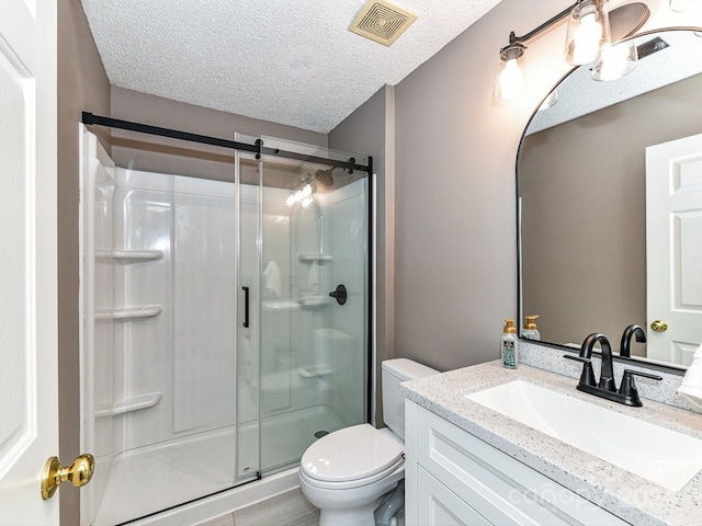 bathroom featuring a textured ceiling, vanity, toilet, and a shower with shower door