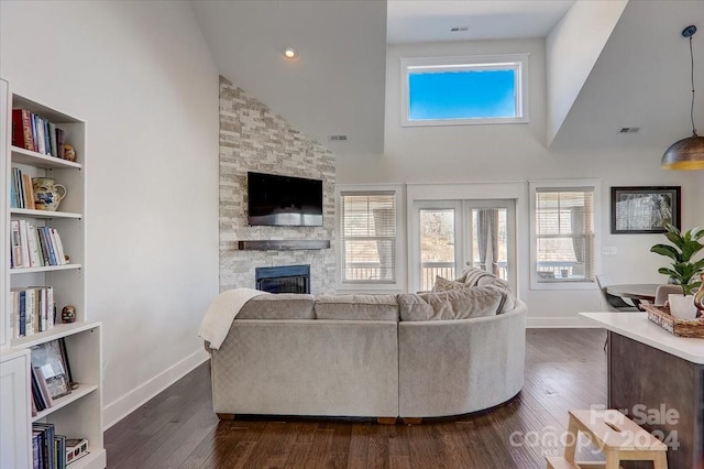 living room featuring dark hardwood / wood-style floors, high vaulted ceiling, and a stone fireplace