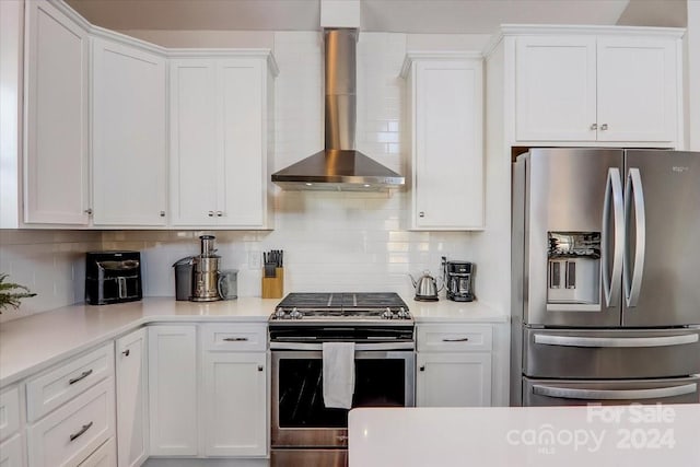 kitchen with white cabinets, appliances with stainless steel finishes, decorative backsplash, and wall chimney range hood