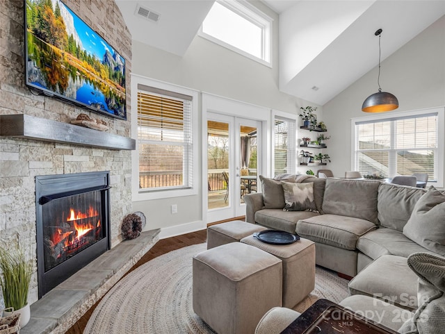 living room with a stone fireplace, high vaulted ceiling, french doors, and hardwood / wood-style flooring