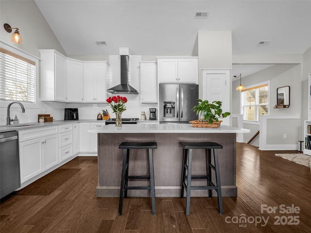 kitchen with wall chimney range hood, sink, appliances with stainless steel finishes, white cabinetry, and a center island