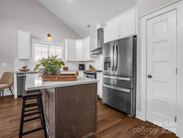 kitchen with white cabinetry, stainless steel appliances, a center island, a kitchen bar, and wall chimney exhaust hood