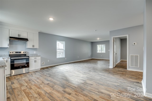 kitchen with stainless steel range with electric cooktop, light stone countertops, light wood-type flooring, and white cabinetry