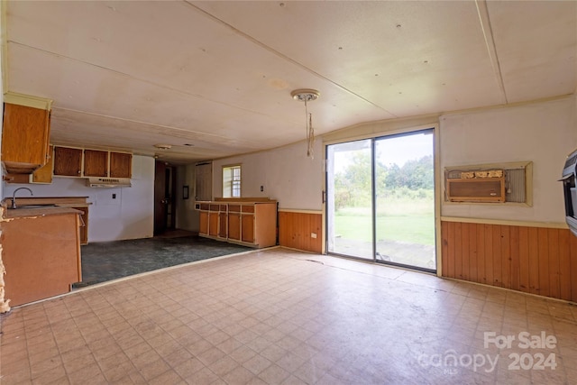 kitchen with lofted ceiling, wood walls, sink, and decorative light fixtures