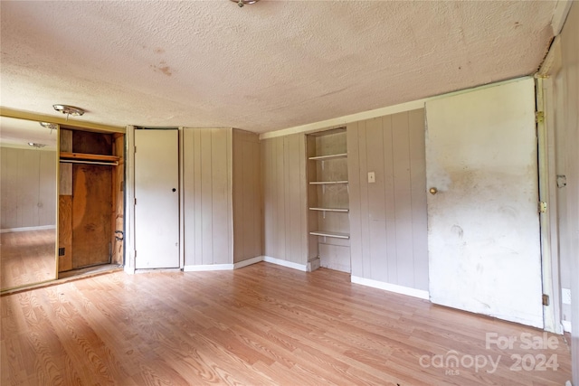 unfurnished bedroom with light wood-type flooring, a textured ceiling, wooden walls, and a closet