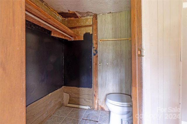 bathroom featuring a textured ceiling, wood walls, and toilet