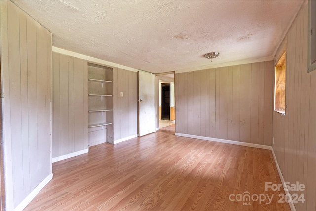 unfurnished room featuring wood-type flooring, a textured ceiling, and wooden walls