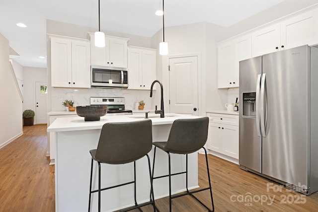 kitchen with appliances with stainless steel finishes, decorative light fixtures, white cabinetry, sink, and a kitchen island with sink