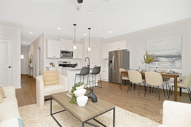 living room featuring ceiling fan, sink, and light hardwood / wood-style floors