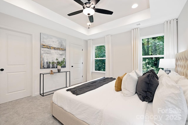 carpeted bedroom featuring ceiling fan and a tray ceiling