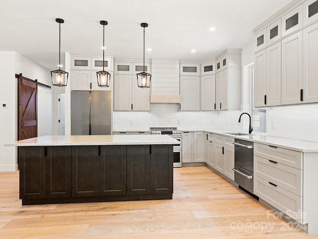 kitchen with light wood-type flooring, stainless steel appliances, a kitchen island, sink, and a barn door