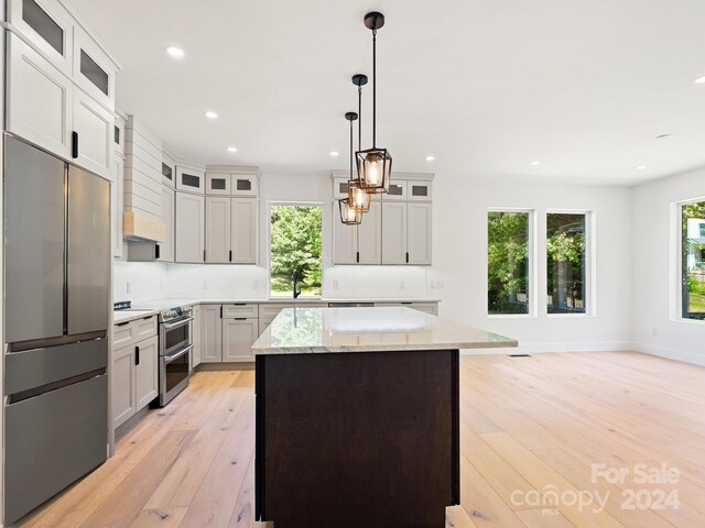 kitchen featuring a center island, light hardwood / wood-style flooring, decorative light fixtures, stainless steel appliances, and white cabinetry