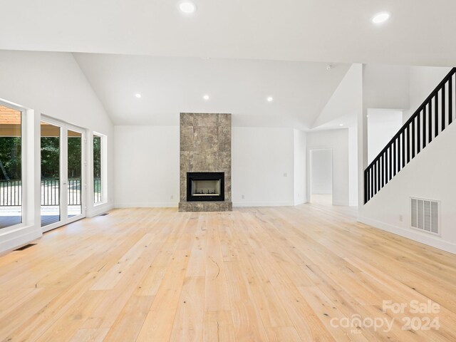 unfurnished living room with a tiled fireplace, high vaulted ceiling, and light hardwood / wood-style floors