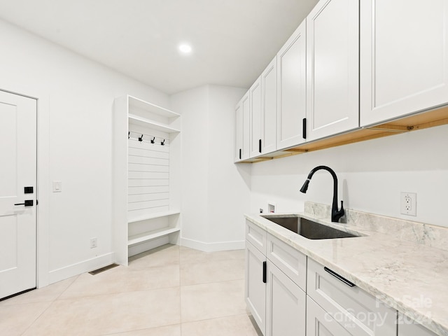 interior space featuring light tile patterned floors, sink, light stone countertops, and white cabinets