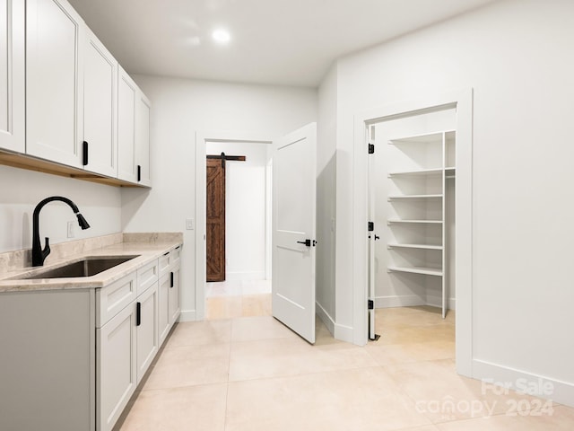 kitchen featuring a barn door, light tile patterned flooring, sink, light stone countertops, and white cabinets