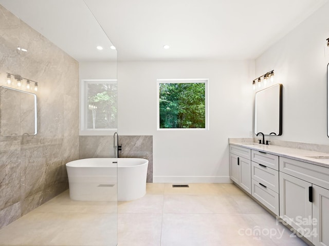 bathroom with tile patterned floors, tile walls, a bathtub, and vanity