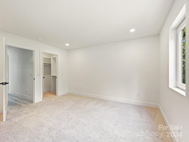 unfurnished bedroom featuring a spacious closet, light colored carpet, and a closet