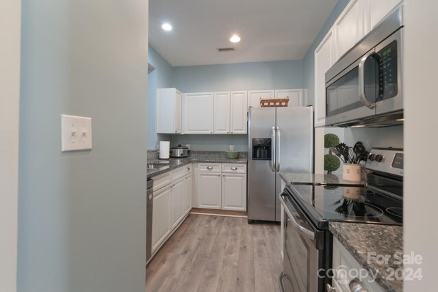 kitchen featuring light hardwood / wood-style flooring, appliances with stainless steel finishes, dark stone counters, and white cabinetry