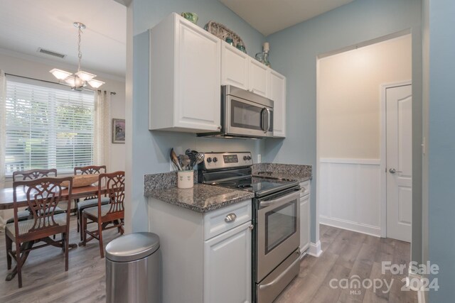 kitchen with appliances with stainless steel finishes, light hardwood / wood-style floors, white cabinets, an inviting chandelier, and dark stone counters