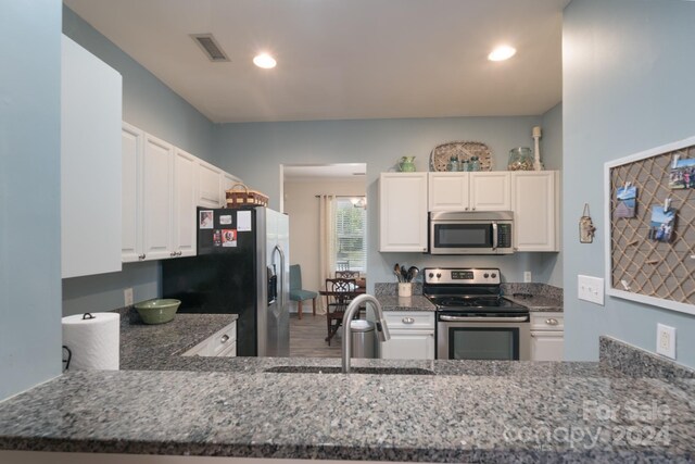 kitchen featuring appliances with stainless steel finishes, white cabinets, kitchen peninsula, dark stone counters, and sink