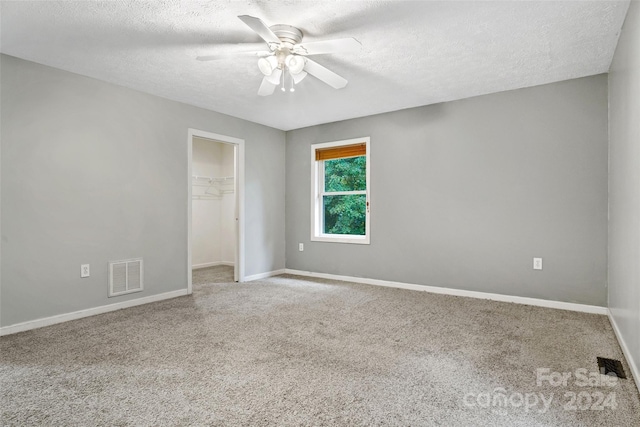 unfurnished bedroom with ceiling fan, a textured ceiling, carpet, a closet, and a spacious closet