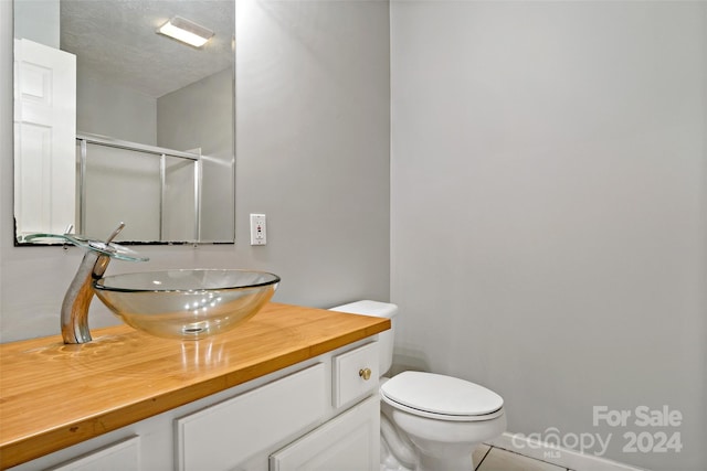 bathroom with vanity, a textured ceiling, a shower with shower door, tile patterned floors, and toilet